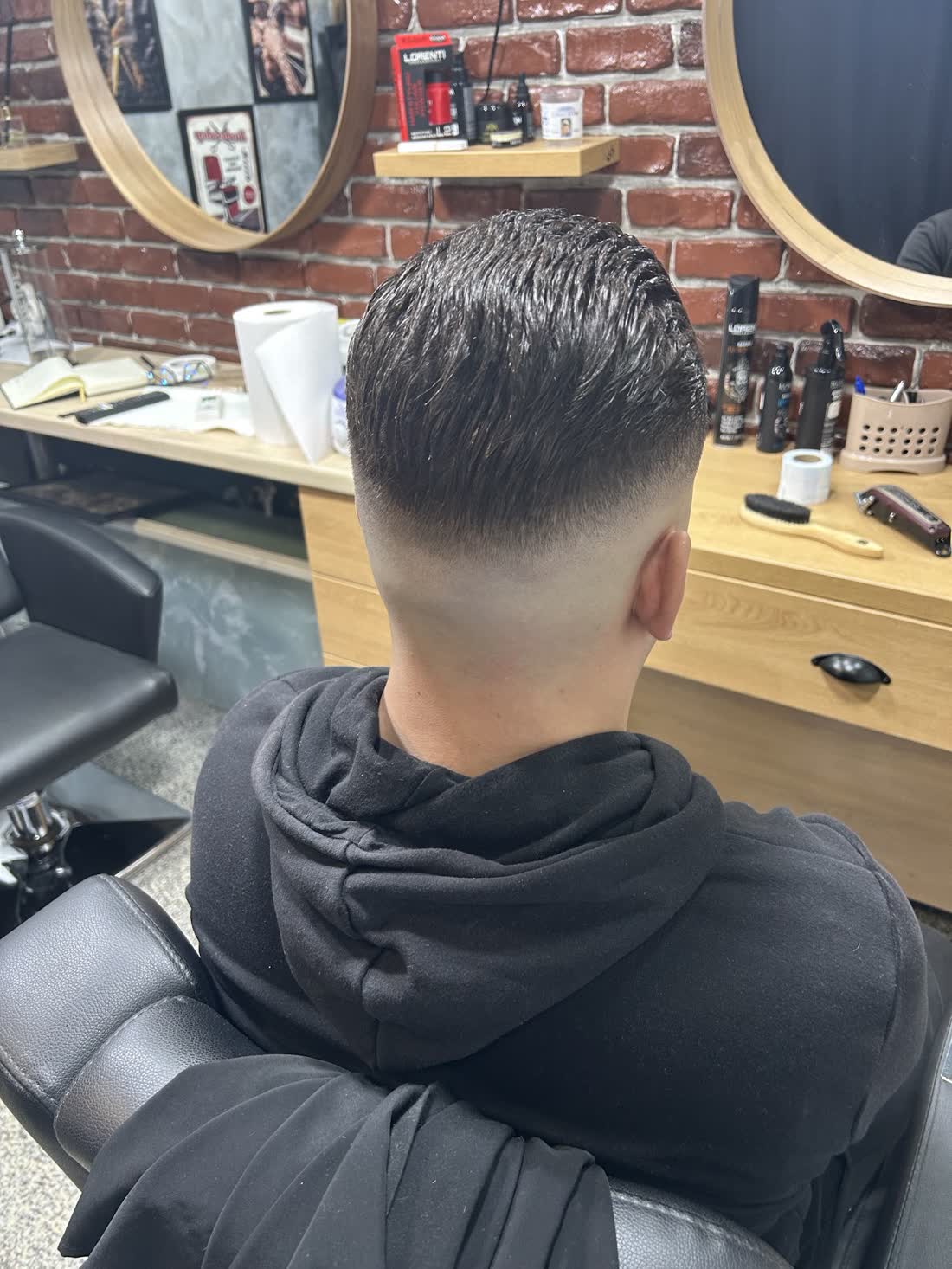 Taper fade văzut din spate, lângă peretele de cărămidă